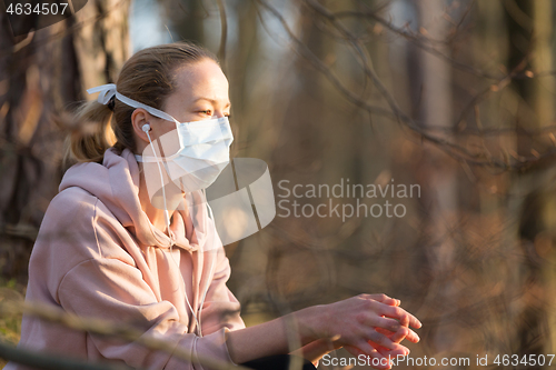 Image of Portrait of caucasian sporty woman wearing medical protection face mask while relaxing in nature and listening to music. Corona virus, or Covid-19, is spreading all over the world