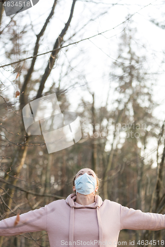 Image of Portrait of caucasian sporty woman wearing medical protection face mask while relaxing by taking a deep breath in forest. Corona virus, or Covid-19, is spreading all over the world