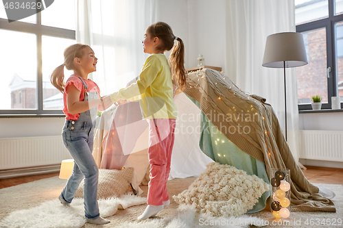 Image of happy girls playing near kids tent at home