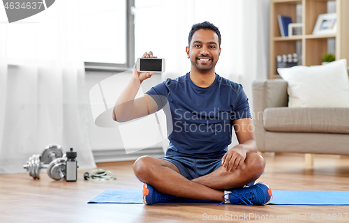 Image of indian man with smartphone on exercise mat at home