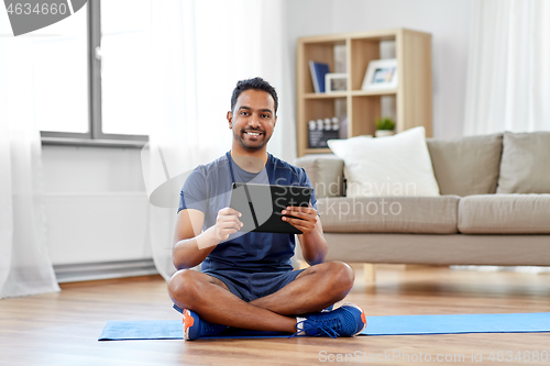 Image of indian man with tablet pc and exercise mat at home