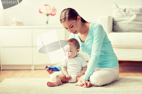 Image of happy mother showing smartphone to baby at home