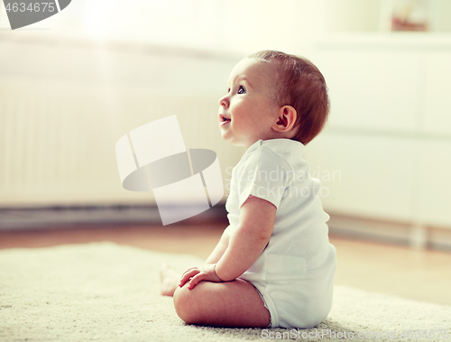 Image of happy baby boy or girl sitting on floor at home