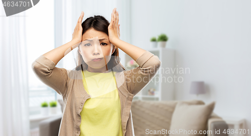 Image of stressed asian woman holding to her head at home