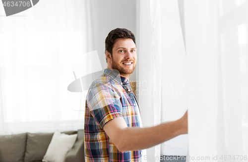 Image of young man opening window curtain at home