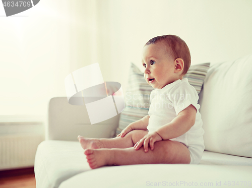 Image of happy baby boy or girl sitting on sofa at home