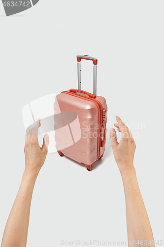 Image of Woman hands try to take travel suitcase on a light grey background.