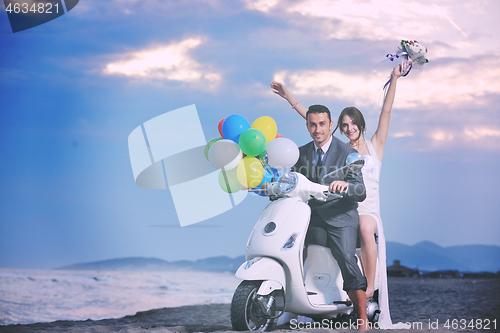 Image of just married couple on the beach ride white scooter