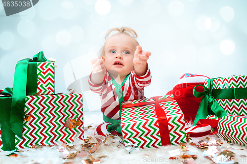 Image of Cute baby girl 1 year old near santa hat posing over Christmas background. Sitting on floor with Christmas ball. Holiday season.