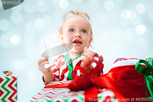 Image of Cute baby girl 1 year old near santa hat posing over Christmas background. Sitting on floor with Christmas ball. Holiday season.