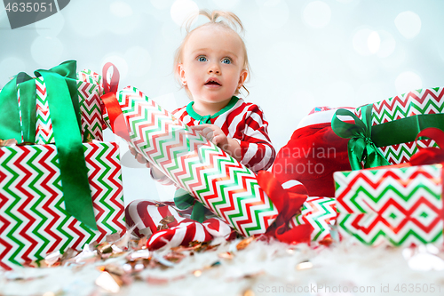 Image of Cute baby girl 1 year old near santa hat posing over Christmas background. Sitting on floor with Christmas ball. Holiday season.