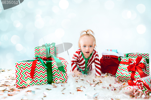 Image of Cute baby girl 1 year old near santa hat posing over Christmas background. Sitting on floor with Christmas ball. Holiday season.