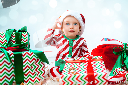 Image of Cute baby girl 1 year old wearing santa hat posing over Christmas background. Sitting on floor with Christmas ball. Holiday season.