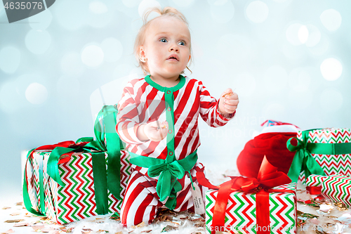 Image of Cute baby girl 1 year old near santa hat posing over Christmas background. Sitting on floor with Christmas ball. Holiday season.