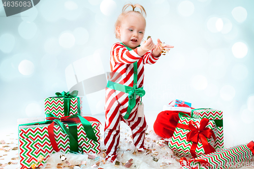 Image of Cute baby girl 1 year old wearing santa hat posing over Christmas background. Sitting on floor with Christmas ball. Holiday season.