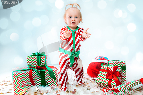 Image of Cute baby girl 1 year old wearing santa hat posing over Christmas background. Sitting on floor with Christmas ball. Holiday season.