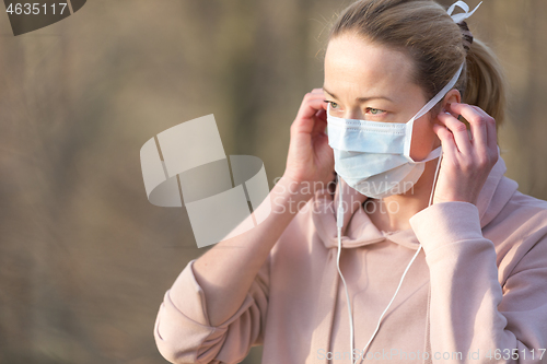 Image of Portrait of caucasian sporty woman wearing medical protection face mask while walking in park, relaxing and listening to music. Corona virus, or Covid-19, is spreading all over the world