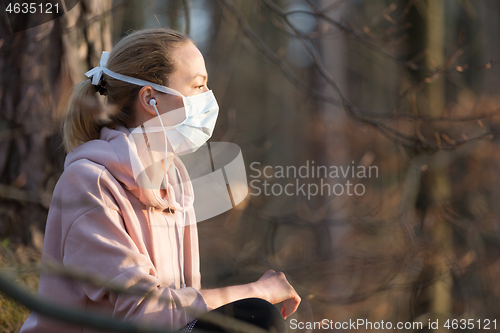 Image of Portrait of caucasian sporty woman wearing medical protection face mask while relaxing in nature and listening to music. Corona virus, or Covid-19, is spreading all over the world