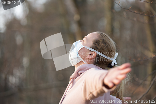 Image of Portrait of caucasian sporty woman wearing medical protection face mask while relaxing by taking a deep breath in forest. Corona virus, or Covid-19, is spreading all over the world