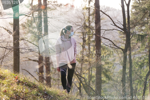 Image of Corona virus, or Covid-19, is spreading all over the world. Portrait of caucasian sporty woman wearing a medical protection face mask while walking in the forest. Corona virus.