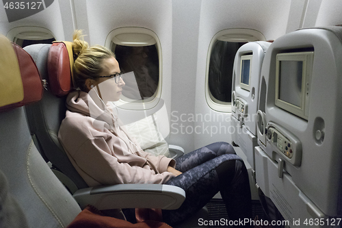 Image of Sporty casual young blonde caucasian lady watching movie while traveling by airplane by the window. Commercial transportation by planes