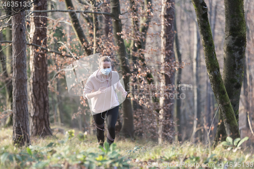 Image of Corona virus, or Covid-19, is spreading all over the world. Portrait of caucasian sporty woman wearing a medical protection face mask while running in nature.