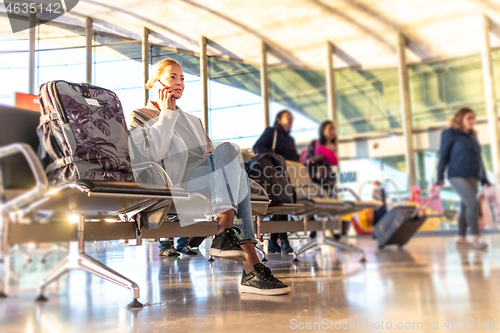 Image of Casual blond young woman using her cell phone while waiting to board a plane at bussy airport departure gates.