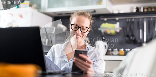 Image of Stay at home and social distancing. Woman in her casual home clothing working remotly from her kitchen dining table in the morning. Video chatting with friend, family or business clients or partners