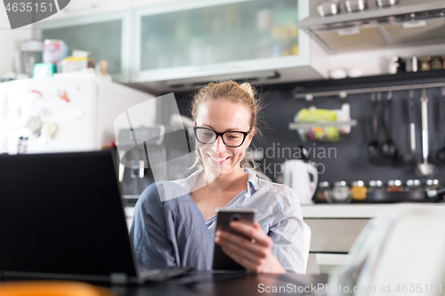 Image of Stay at home and social distancing. Woman in her casual home clothing working remotly from her kitchen dining table in the morning. Video chatting with friend, family or business clients or partners