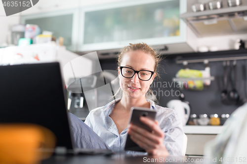 Image of Stay at home and social distancing. Woman in her casual home clothing working remotly from her kitchen dining table in the morning. Video chatting with friend, family or business clients or partners