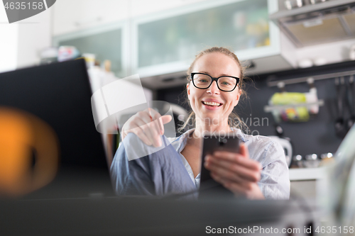 Image of Stay at home and social distancing. Woman in her casual home clothing working remotly from kitchen dining table. Video chatting using social media with friend, family, business clients or partners