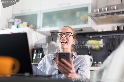 Image of Stay at home and social distancing. Woman in her casual home clothing working remotly from kitchen dining table. Video chatting using social media with friend, family, business clients or partners