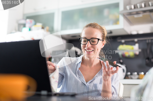 Image of Stay at home and social distancing. Woman in her casual home clothing working remotly from kitchen dining table. Video chatting using social media with friend, family, business clients or partners