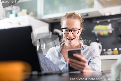 Image of Stay at home and social distancing. Woman in her casual home clothing working remotly from kitchen dining table. Video chatting using social media with friend, family, business clients or partners