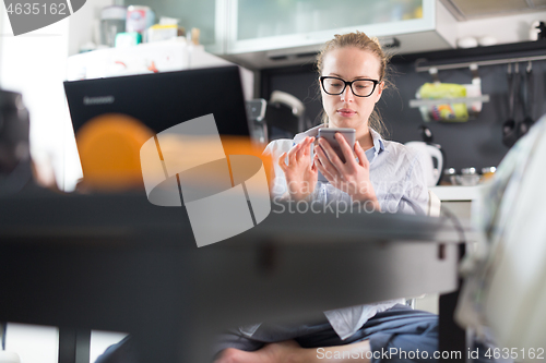 Image of Stay at home and social distancing. Woman in her casual home clothing working remotly from kitchen dining table. Video chatting using social media with friend, family, business clients or partners