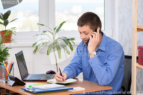 Image of Office employee with a smile talking on the phone and writes in a diary