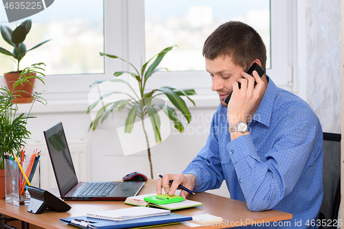 Image of An office employee is smiling on the phone and counting on a calculator