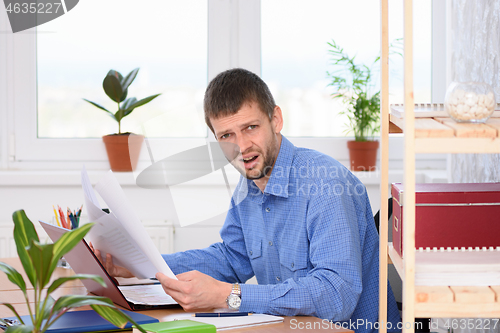 Image of The office employee in a shocked state reads business papers and looked into the frame.