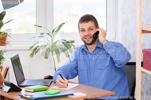 Image of An office employee is talking on the phone with a smile and looked in frame