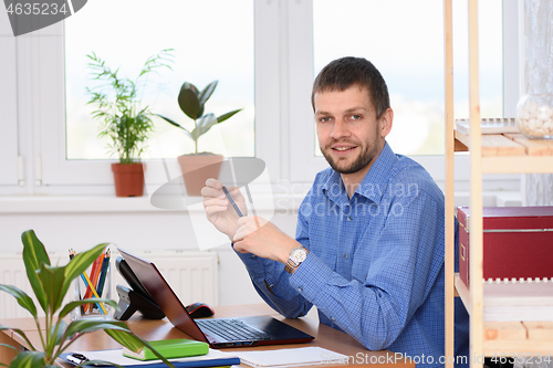 Image of Business office worker sits at a table in the office and holds a pen in his hands