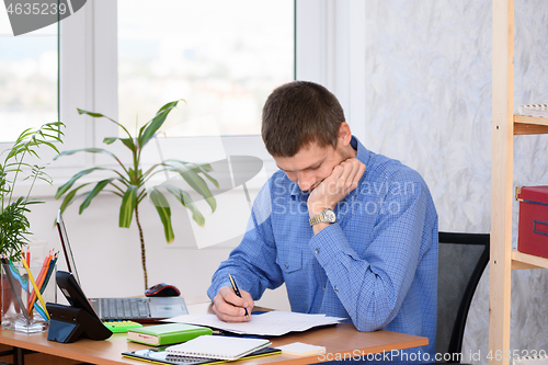Image of Pensive employee reads business papers in the office