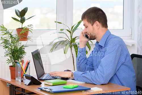 Image of The specialist in the office works at the computer and talks on the phone