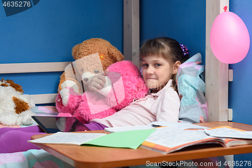 Image of Girl\'s lip lying on the bed with soft toys and textbooks in the foreground