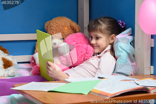 Image of Nine-year-old girl lies on bed with toys and looks at tablet