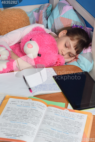Image of Girl fell asleep in a hug with a teddy bear doing lessons at home