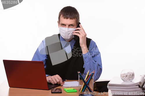 Image of The clerk in a medical mask is talking on the phone and looked in the frame