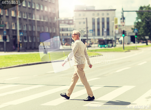 Image of senior man walking along city crosswalk