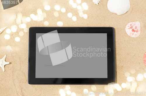 Image of tablet computer and seashells on beach sand