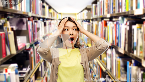 Image of stressed asian woman holding to head at library