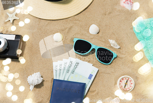 Image of money in passport, shades and hat on beach sand